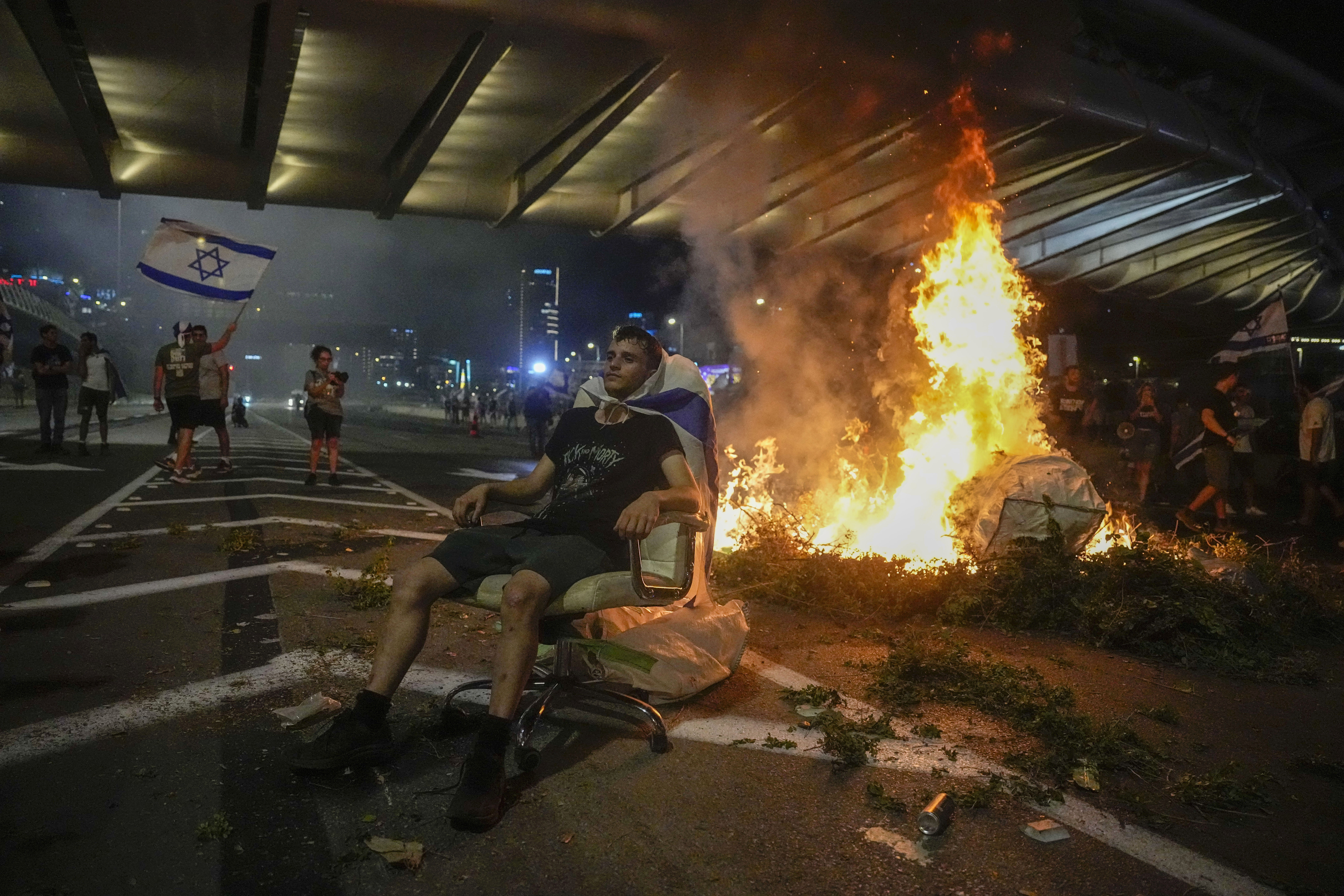 A bonfire burns as Israelis occupy the Ayalon Highway to protest against plans by Prime Minister Benjamin Netanyahu's government to overhaul the judicial system, in Tel Aviv, Thursday, July 20, 2023. (AP Photo/Ariel Schalit)