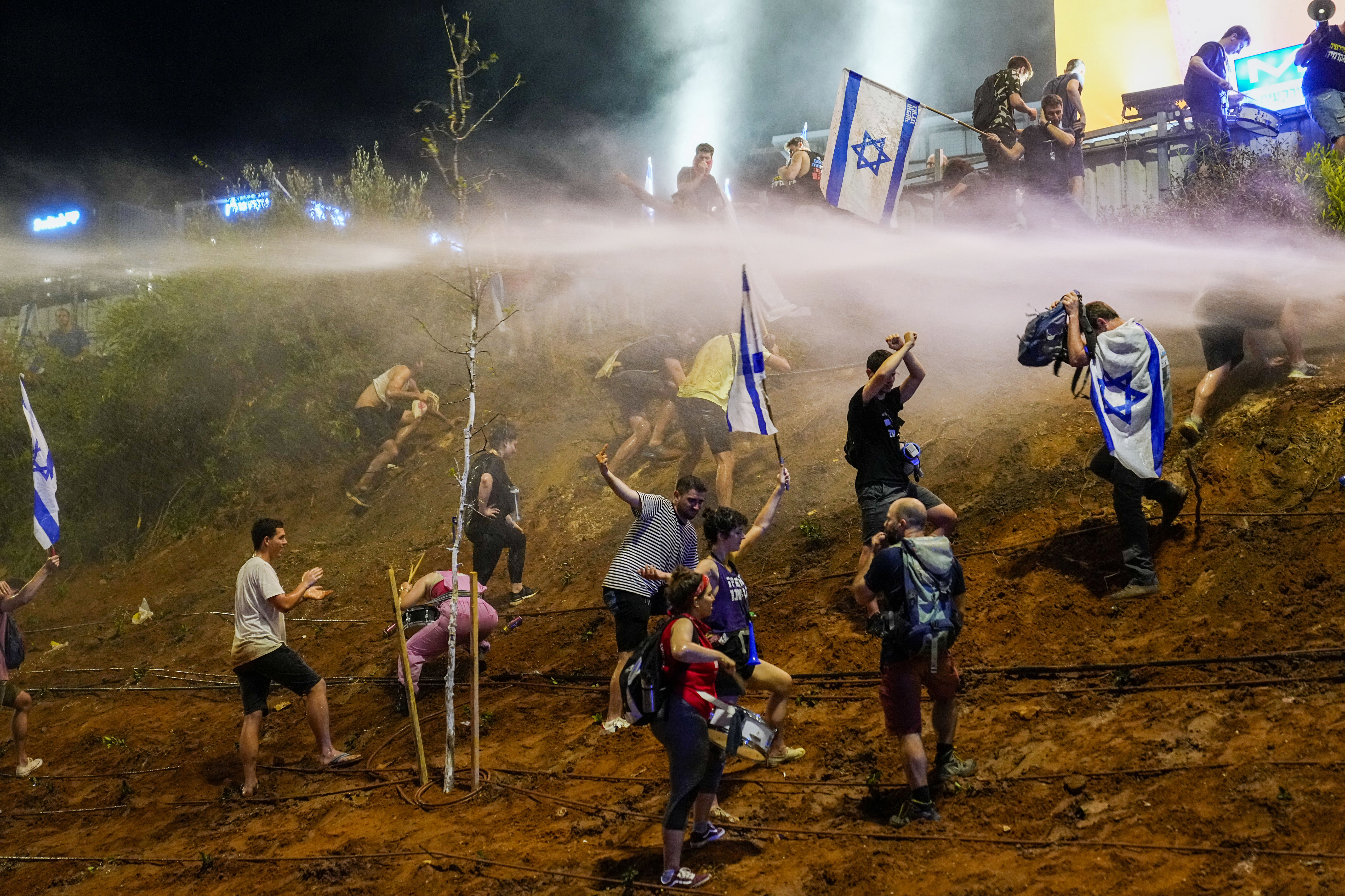 EDS NOTE: OBSCENITY - Israeli police use a water cannon to disperse demonstrators blocking a highway during a protest against plans by Prime Minister Benjamin Netanyahu's government to overhaul the judicial system, in Tel Aviv, Israel, Thursday, July 20, 2023. (AP Photo/Ohad Zwigenberg)