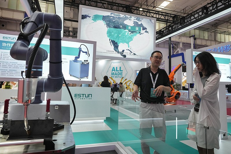 An exhibitor talks to a visitor at a booth displaying industrial robotic arms with a screen showing a U.S. map during the annual World Robot Conference at the Etrong International Exhibition and Convention Center in Beijing on Thursday.
(AP/Andy Wong)