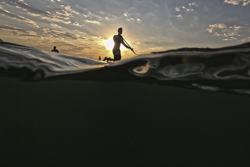 A man floats on a paddle board off Copacabana beach in Rio de Janeiro, Brazil at sunrise Thursday, Aug. 24, 2023. Brazil is facing a heat wave during the southern hemisphere's winter. (AP Photo/Bruna Prado)