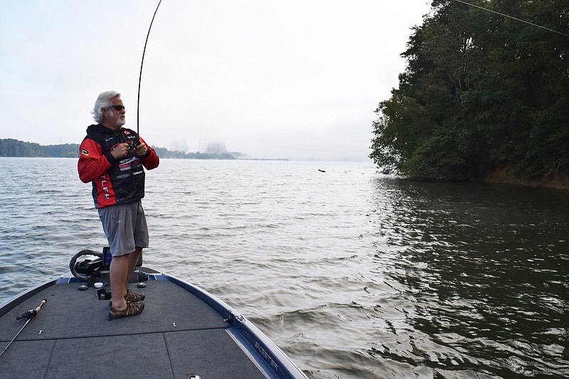 Staff Photo by Ben Benton / As Sequoyah Nuclear Plant's cooling towers appear through the fog Friday, Gene Elkins, of Pacific, Mo., reels in his lure on Chickamauga Lake. Elkins planned to take his daughter, who lives minutes from Harrison Bay State Park, fishing for the weekend.