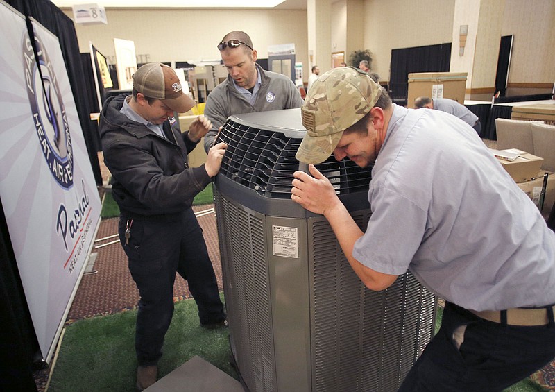 Andrew Bryant (from left), service technician, Charley Boyce, owner, and Hayden Williams, service technician, with Paschal Heat, Air and Geothermal of Springdale, move an outdoor air conditioning unit into position for display Thursday, February 11, 2016 for the NWA Homeshow at the Northwest Arkansas Convention Center in Springdale. (NWA Democrat-Gazette/DAVID GOTTSCHALK )