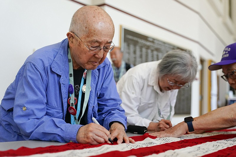 Paul Tomita (left), survivor of the Minidoka interment camp in World War I, and wife Mabel, a survivor of Tule Lake and Gila River, sign a World War II-era 48-star flag at the College of Southern Idaho on July 7 in Twin Falls, Idaho.
(AP/Lindsey Wasson)