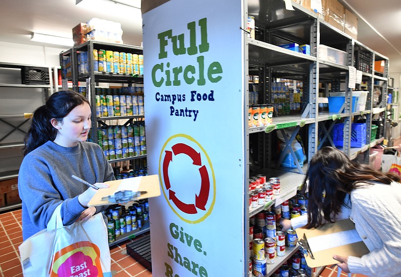 Emma Johnson (left), a University of Arkansas, Fayetteville student from Siloam Springs, collects items while volunteering to fill orders from the Jane B. Gearhart Full Circle Campus Food Pantry in this March 13, 2023 file photo. The pantry offers three days of food assistance up to two times per week for anyone affiliated with either the UA campus or the University of Arkansas for Medical Sciences Northwest campus. Volunteers accept and distribute food donations. (NWA Democrat-Gazette/Andy Shupe)