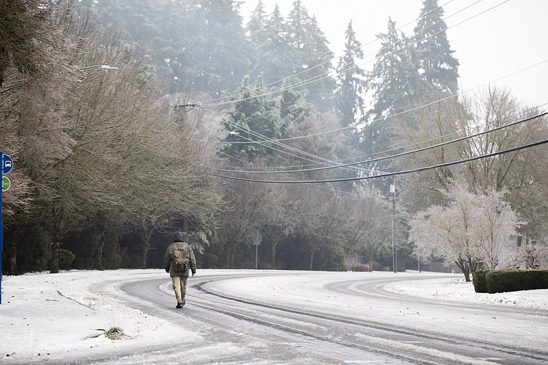 A man walks on the road in the snow on Wednesday, Jan. 17, 2024, in Tigard, Ore. An ice storm threatened to topple towering trees onto power lines and turned mountain highways treacherous Wednesday in the Pacific Northwest, where residents were urged to avoid travel. (AP Photo/Jenny Kane)