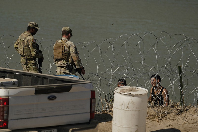 National Guardsmen talk with migrants trying to cross the Rio Grande from Mexico into the United States near Eagle Pass, Texas, in this July 11, 2023 file photo. Texas Republican Gov. Greg Abbott's use of razor wire along the border has become a point of contention with President Joe Biden's administration. (AP/Eric Gay)