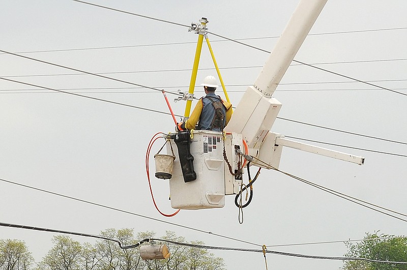 A lineman uses a bucket lift to support three power lines during repairs to a nearby electric pole in this April 18, 2011 file phot. (NWA Democrat-Gazette file photo)