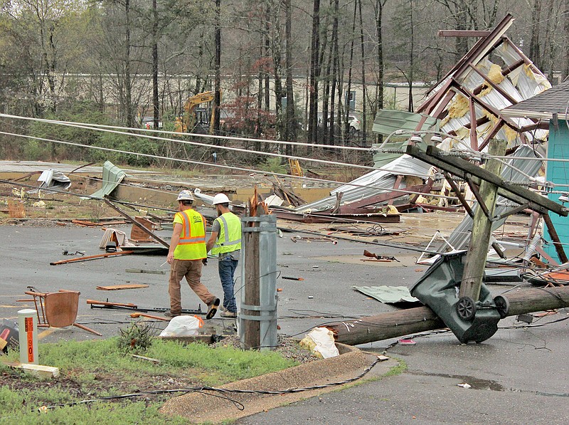 Utility workers walk past a trash bin that is impaled by the remnants of a utility pole in the 3900 block of Arkansas Highway 7 north Friday. (The Sentinel-Record/James Leigh)