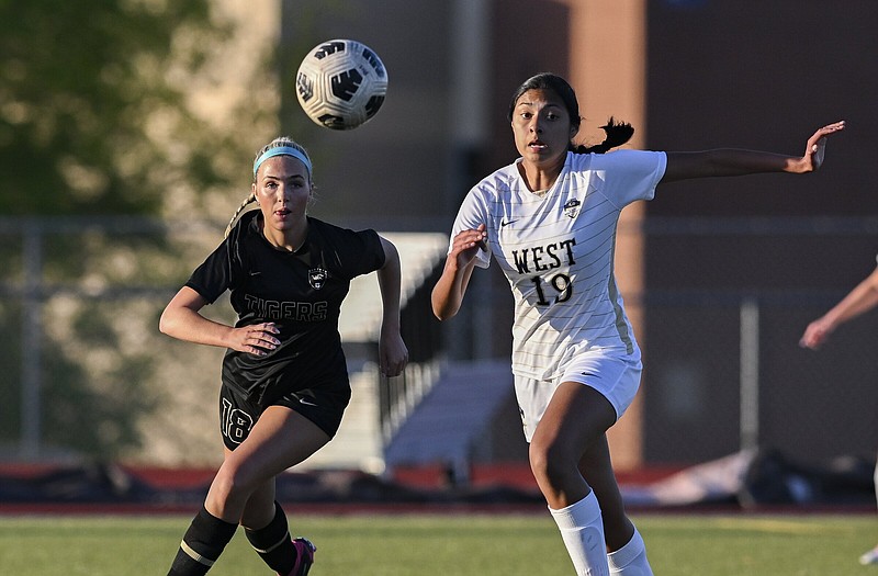 Bentonville defender Ashby Burnett (18) and Bentonville West Rihanna Andrade (19) approach the ball Friday, April 12, 2024 during a soccer game at Tiger Athletic Complex at Bentonville High School in Bentonville. Visit nwaonline.com/photos for today's photo gallery...(NWA Democrat-Gazette/Charlie Kaijo)
