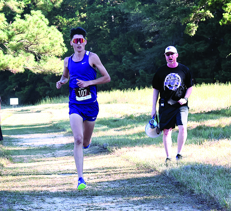 El Dorado's Zachary McMillon, with encouragement from Coach John Koonce, runs with a big lead during the El Dorado Wildcat Invitational Saturday morning at South Arkansas Regional Airport. McMillon led the Wildcats to a victory at the meet.