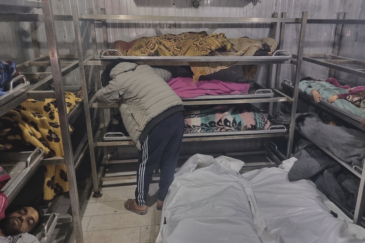 A man mourns over the body of a child, lying among other victims at the hospital morgue, following Israeli airstrikes in Khan Younis, southern Gaza Strip, Tuesday, March 18, 2025. (AP Photo/Mohammad Jahjouh)