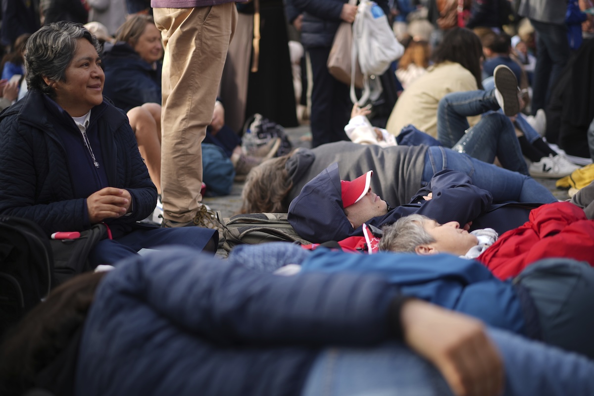 Faithful rest on the ground ahead of the funeral of Pope Francis in St. Peter's Square at the Vatican, Saturday, April 26, 2025. (AP Photo/Andrew Medichini)