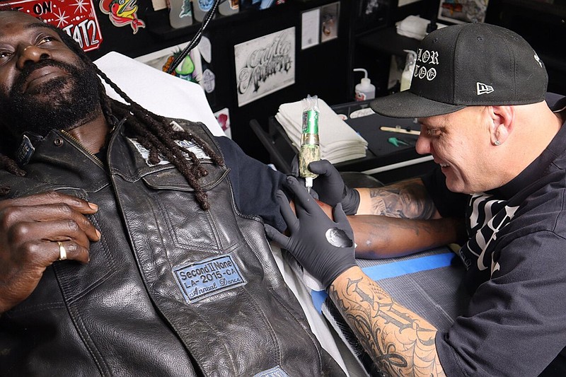 The Parlor owner and tattoo artist Josh Chambers demonstrates his wireless rotary tattoo machine on John Shackleford in the 22 May 2025 photo. (Arkansas Democrat-Gazette/Jesse Cain)