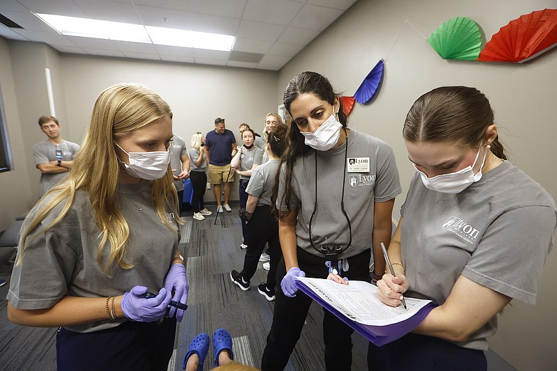 Lyon College dental students Anna Grace Ludwig (left) and Kaitlin Parker (right) look over a patient’s chart with Dr. Sandie Leding (left) during Give Kids a Smile Day on Friday, July 18, 2025, hosted by Lyon College School of Dental Medicine in Little Rock. .(Arkansas Democrat-Gazette/Thomas Metthe)