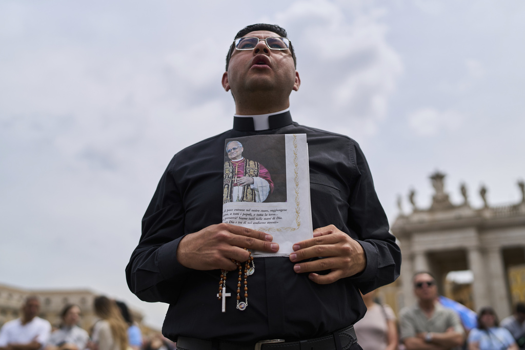 A priest holds a rosary and a newspaper showing a picture of Pope Leo XIV as he appears May 11, 2025, at the central balcony of St. Peter's Basilica for his first Sunday blessing after his election, in St. Peter's Square at the Vatican. (AP Photo/Bernat Armangue)