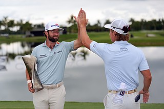 Cameron Young holds the tournament trophy Sunday as he celebrates with his caddie after winning the PGA Tour's Cadillac Championship on the Blue Monster Course in Doral, Fla. (AP Photo/David J. Phillip)