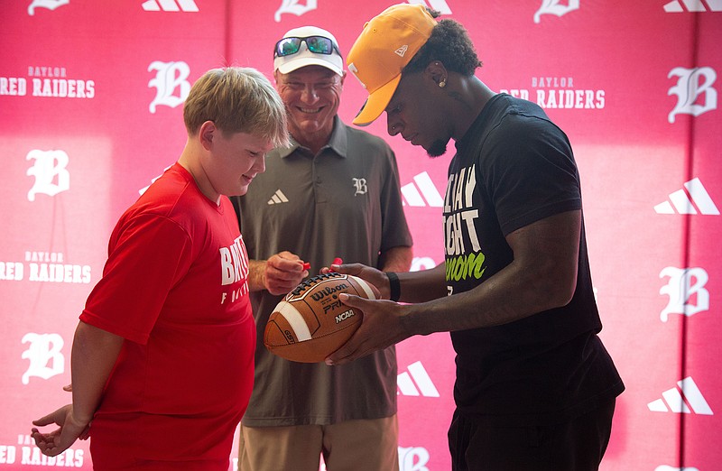 Staff photo by Larry Sullivan II/David Gabriel Georges, right, signs a football at his commitment ceremony at the Baylor Probasco Academic Center on July 22, 2026.