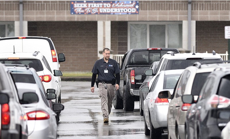 Staff Photo by Robin Rudd / In the rain, Hamilton County Schools student security officer Victor Talavera sheperds the traffic as people line up to receive technology for their children to use at home.  Essential technology was issued to families at East Ridge Elementary on March 20, 2020.