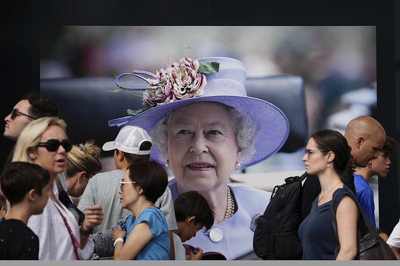 Passers by walk in front of a picture of Queen Elizabeth II, in London, Sunday, Sept. 11, 2022. Queen Elizabeth II, Britain's longest-reigning monarch and a rock of stability across much of a turbulent century, died Thursday Sept. 8, 2022, after 70 years on the throne. She was 96. (AP Photo/Christophe Ena)