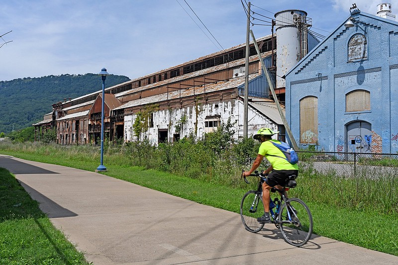 Staff Photo by Robin Rudd / A bicyclist uses the Tennessee Riverwalk as he passes the former U.S. Pipe/Wheland Foundry site on June 14, 2022. The former foundry property is to hold a new stadium for the Chattanooga Lookouts and other development.