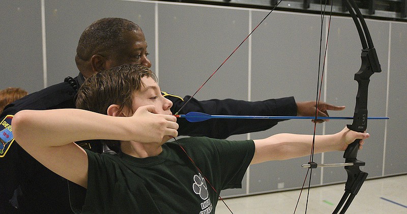 Staff File Photo By Matt Hamilton / School resource officer Mike Houston helps guide Logan Mabry, 11, as he aims an arrow during archery practice at Lofts Middle School in February 2022.