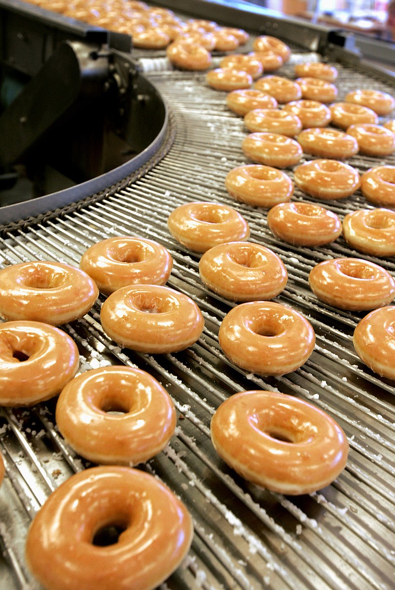 Freshly iced doughnuts roll by on a conveyor belt at a Krispy Kreme store in Winston-Salem, N.C., on Jan. 14, 2005. Krispy Kreme is among the businesses offering free food to veterans and active-duty military personnel on Veterans Day. / AP Photo/File/Kim Walker