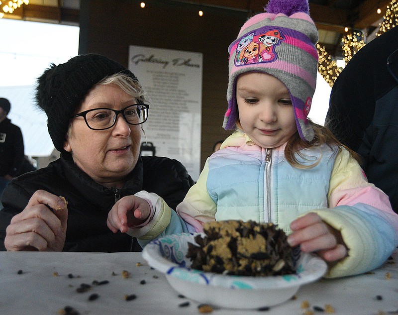 Staff photo by Matt Hamilton / Dressed for the cold, Collegedale resident Monica Rek helps her granddaughter Naomi Rudder, 5, make a pinecone covered in seeds at the Bird Shoppe booth during the Christmas in Collegedale event on Sunday.