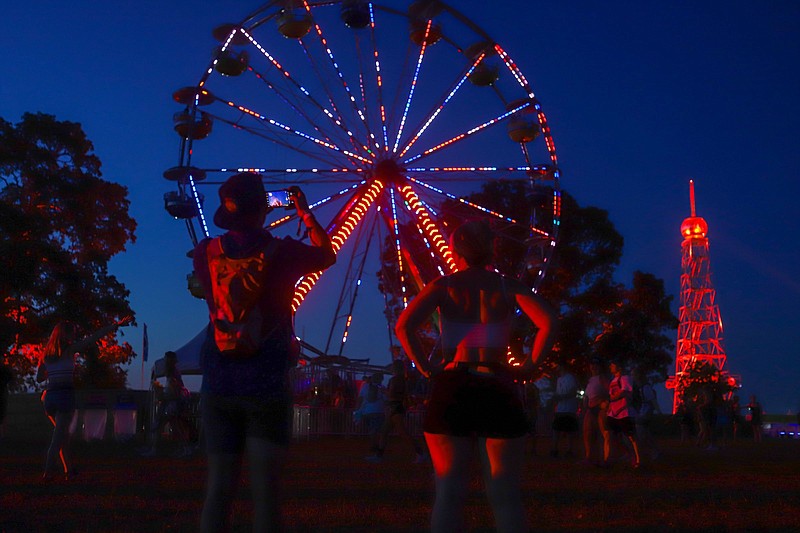 Staff photo by Olivia Ross  / A couple takes a photo of the illuminated ferris wheel at Bonnaroo on June 16, 2022. The 2023 lineup was released Tuesday.