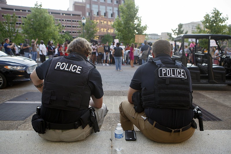 Staff photo by C.B. Schmelter / Two police officers sit as protesters stand across Georgia Avenue from them on Monday, June 1, 2020 in Chattanooga, Tenn. They were protesting the death of George Floyd. Floyd, 46, died after being handcuffed and pinned for several minutes beneath Minneapolis police Officer Derek Chauvin's knee. Protests entered their third night in Chattanooga.