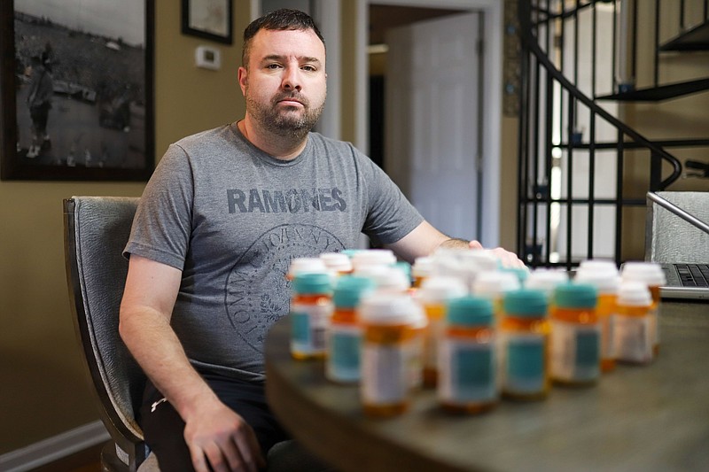 Staff photo by Olivia Ross  / Doug Frizzell sits in his home, various medications he has been prescribed sit in front of him on Wednesday, February 22, 2023. Frizzell has been experiencing long COVID symptoms for nearly two years.