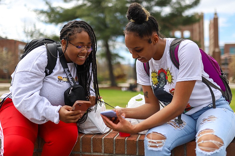 Staff photo by Olivia Ross / Aniya Flournoy and Kennedy Rawls laugh at a post on their phones as they sit outside at UT Chattanooga on Thursday, March 23, 2023.