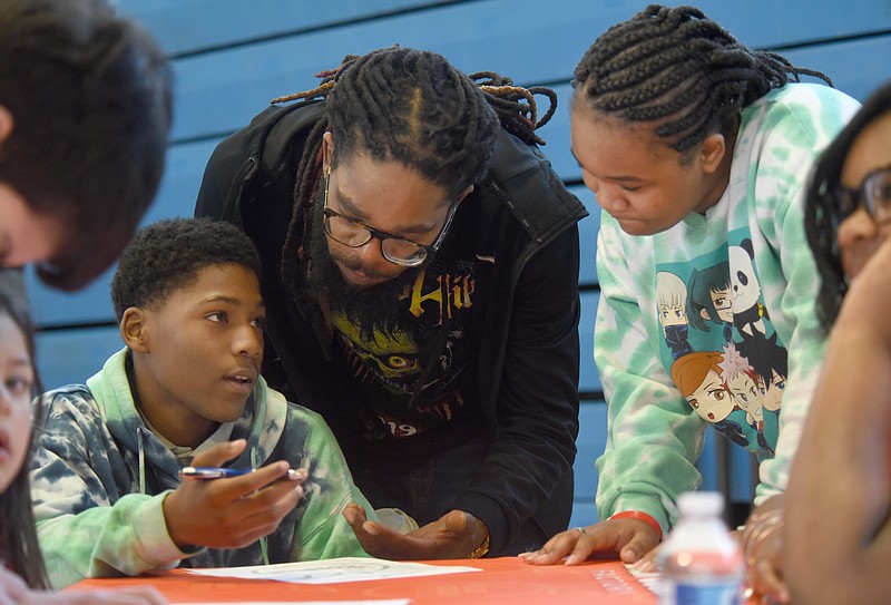 Staff Photo by Matt Hamilton / Brian Strickland, middle, helps his son Elijah, 14, as he fills out a job application at the Peach Cobbler Factory booth during a job fair at Brainerd High School on March 25. Looking on is Taniya Martin, 13, Elijah’s cousin.