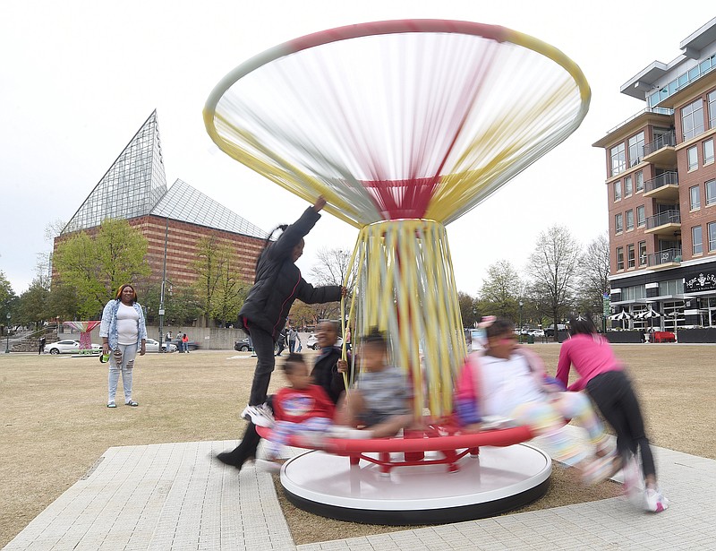 Staff Photo by Matt Hamilton / Chattanooga resident Tonya Upshaw, left, looks on as Starliyah Justice, 7, right, spins children on the Los Trompos interactive art installation at Rock the Riverfront on the Chattanooga Green on March 21. Sunday is the last day to play on the spinning tops.