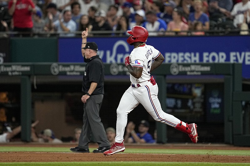 Texas Rangers' Adolis Garcia rounds first as umpire Lance Barksdale signals home run in the fourth inning of a baseball game against the Atlanta Braves, Tuesday, May 16, 2023, in Arlington, Texas. The shot also scored Nathaniel Lowe. (AP Photo/Tony Gutierrez)