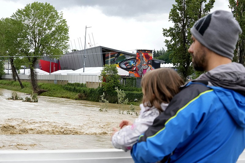 AP photo by Luca Bruno / A man holding a child looks at the swollen Santerno River with the Enzo e Dino Ferrari circuit behind it Wednesday in Imola, Italy. Formula One's Emilia-Romagna Grand Prix, set for Sunday at the track, has been canceled because of the deadly flooding in Italy.
