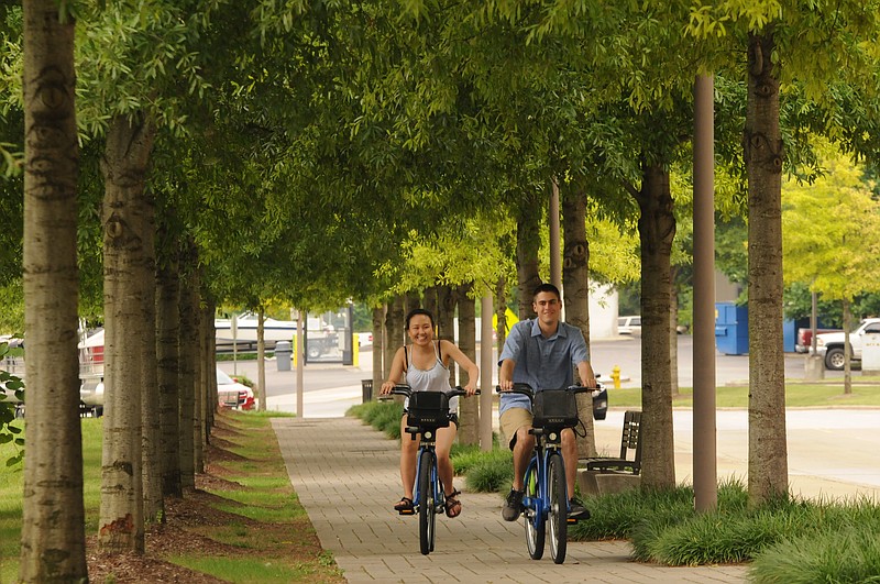 Staff Photo / Mia Han, left, and James Heck ride rental bicycles in a canopy of trees along the 21st Century Riverfront in 2014. Heck was visiting his friend from out of town.