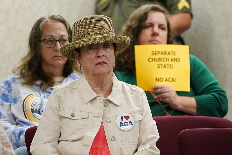 A woman wearing a button supporting charter schools linked to Hillsdale College sits in front of a woman holding a sign opposing the schools during a meeting of the Tennessee Public Charter School Commission staff Sept. 14 in Murfreesboro, Tenn. (AP Photo/Mark Humphrey)
