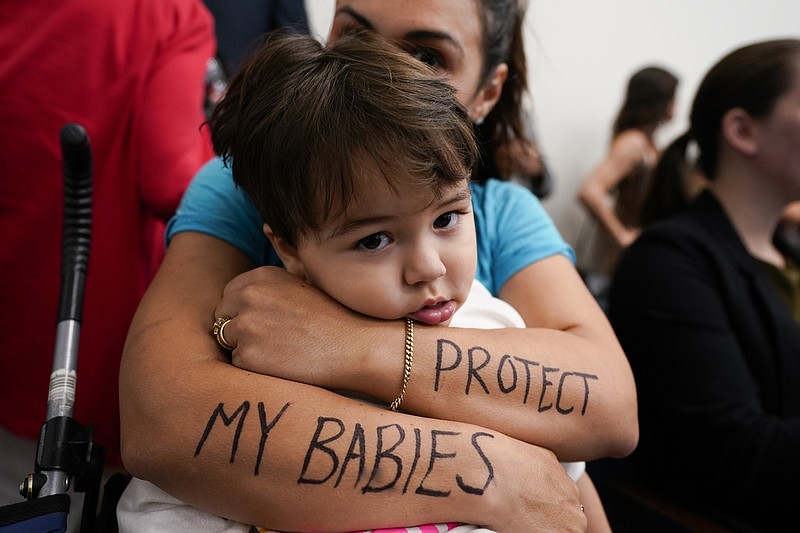 Melissa Alvarez hugs her son Ignacio, 2, with the words "Protect My Babies" written on her arms in the House Civic Justice Committee of 1st Extraordinary Session meeting during a special session of the state legislature on public safety Wednesday, Aug. 23, 2023, in Nashville, Tenn. (AP Photo/George Walker IV)