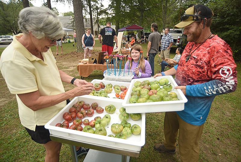 Staff photo by Matt Hamilton/ Matthew Lanier, right, and his daughter Jewel, 6, offer tomatoes to Bevelle Puffer, left, at their booth during a community pancake breakfast and a farmers market held at St. Albans Episcopal Church in Hixson on July 15.
