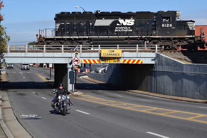 Staff Photo by Ben Benton / As a motorcycle passes underneath, a Norfolk Southern Railway locomotive crosses over Inman Street in Cleveland on Thursday. The overpass has been targeted for removal as part of a railroad crossing elimination project.  Officials said the removal will lend to development of the area and improve traffic.
