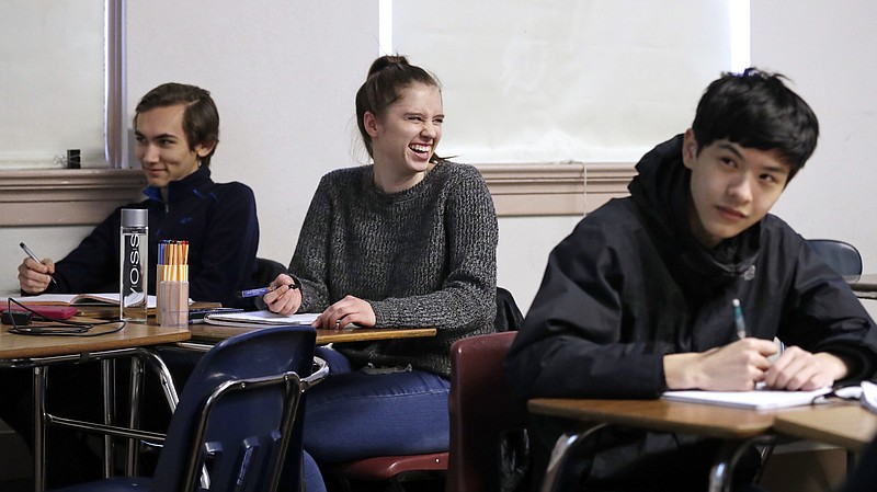 Senior Hazel Ostrowski, center, smiles in 2018 as she looks up during her first period, AP statistics class at Franklin High School in Seattle. High school students are getting more sleep in Seattle, according to a study on later school start times. Ostrowski was among a group at Franklin and another Seattle high school who wore activity monitors to discover whether a later start to the school day would help them get more sleep. It did, adding 34 minutes of slumber a night, and they reported less daytime sleepiness and grades improved. (AP Photo/Elaine Thompson)