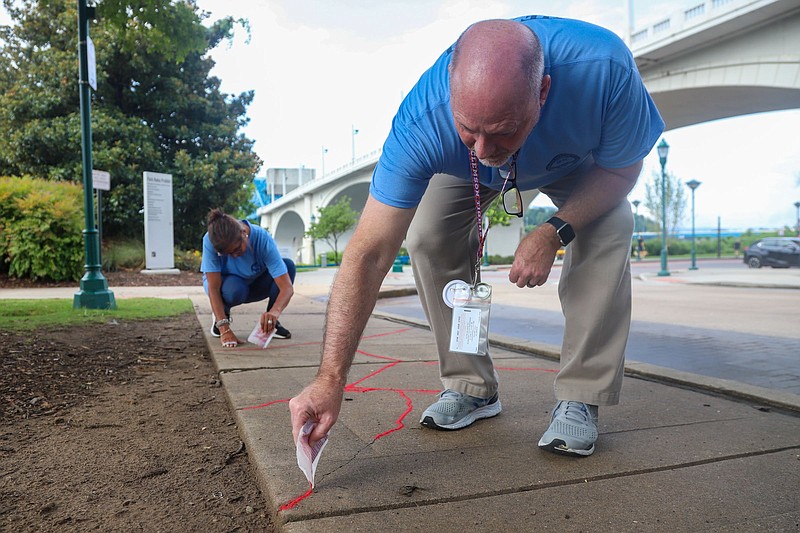 Staff photo by Olivia Ross  / Jeff Malone and Holly Clark fill cracks in the sidewalk at Coolidge Park with sand in 2022. The Tennessee Government Management Institution and the Hamilton County Health Department hosted a Red Sand event to raise awareness about human trafficking. The Red Sand Project states the interactive instillation represents "those individuals who fall through the cracks."