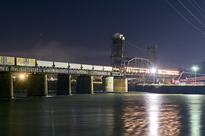 Staff File Photo by Robin Rudd / Lit by the construction lights from the ongoing building of a new lock at Chickamauga Dam, a Norfolk Southern freight train begins to cross the bridge over the Tennessee River, as another train is stopped on the span. Norfolk Southern recently completed the purchase of $453 million worth of property in Hamilton County from the Cincinnati Southern Railway.
