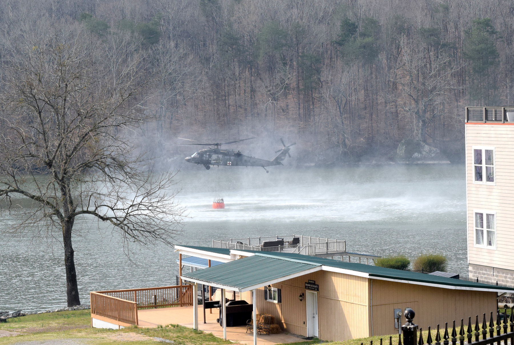 Staff Photo by Ben Benton / A firefighting National Guard helicopter picks up a load of water March 13, 2025, from the Tennessee River to dump on a wildfire in Marion County that has spread across the bluffs north of River Canyon Road at the Hamilton County line. The Chattanooga Air Pollution Control Bureau issued a code orange air quality alert related to smoke from area wildfires.