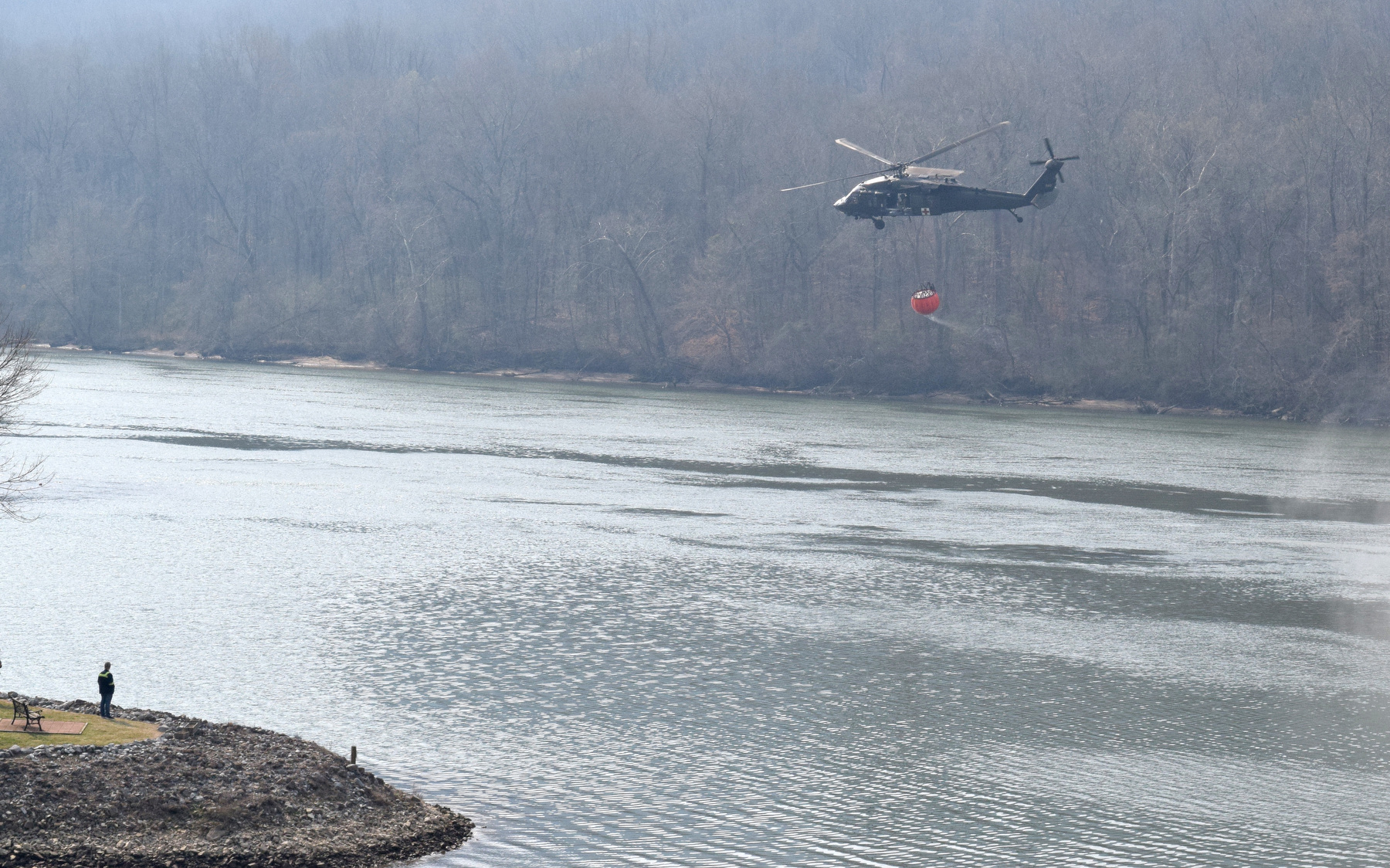 Staff Photo by Ben Benton / A firefighting National Guard helicopter picks up a load of water March 13, 2025, from the Tennessee River to dump on a wildfire in Marion County that has spread across the bluffs north of River Canyon Road at the Hamilton County line. The Chattanooga Air Pollution Control Bureau issued a code orange air quality alert related to smoke from area wildfires.