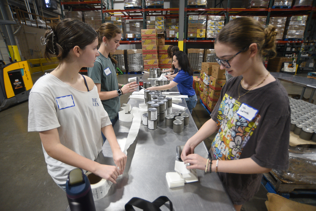 Staff photo by Matt Hamilton/ Volunteers Ally Smith, 14, left, and Della Quattrochi, 15, place labels on cans of cream corn at the Chattanooga Area Food Bank on Friday, April 4, 2025.