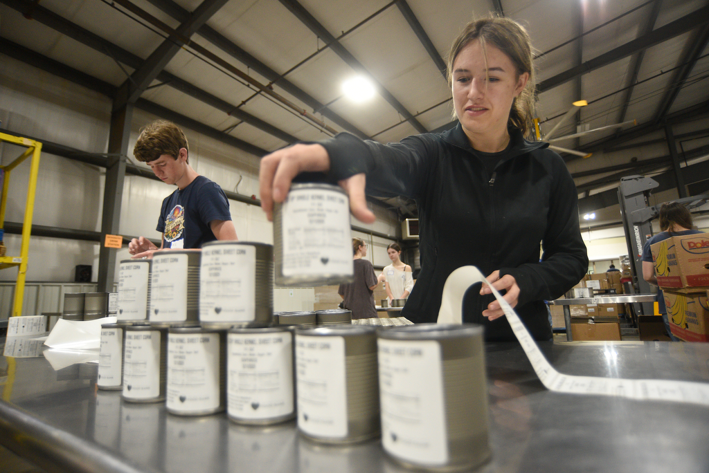 Staff photo by Matt Hamilton/ Volunteers Eli Noles, 16, left, and Zeda Spencer place labels on cans of cream corn at the Chattanooga Area Food Bank on Friday, April 4, 2025.