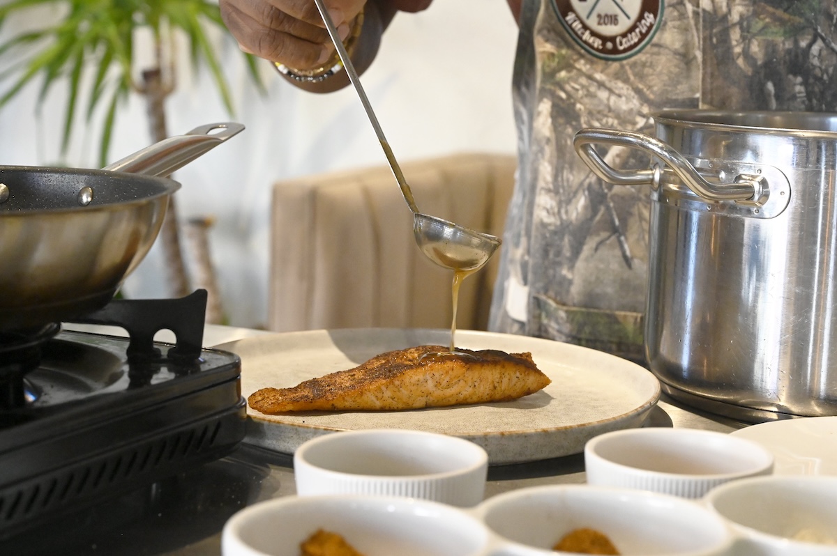 Staff photo by Abby White / Party Bites chef Antonio Tate adds his signature chai bourbon glaze to a salmon fillet.