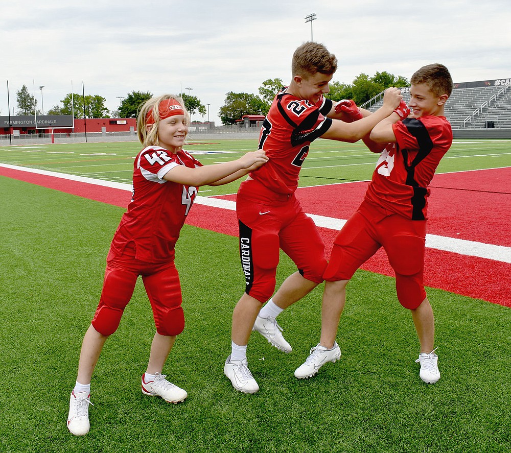 MARK HUMPHREY ENTERPRISE-LEADER/Farmington ninth grader Zane Schmitt (No. 27, 5 feet 11 inches, 175 pounds) who plays linebacker and tight end for the Junior Cardinals, gets his strength tested by his younger brothers, Mason (No. 42, 4 feet 10 inches, 95 pounds) who plays linebacker and tight end for the pee wee team, and Crosby (No. 33, 5 feet 5 inches, 135 pounds), who plays runningback and linebacker for the seventh grade team. The trio are the sons of Steven and Kristen Schmitt. Last week the brothers found opportunity to try out their muscles on somebody else when facing U.S. 62 rival Prairie Grove in the annual 'Battle of 62' al all football levels.
