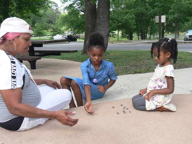 Tina Willis (left) of Hot Springs teaches her granddaughters Syncere and Nylah to play jacks at Hollywood Park in Hot Springs. (Special to the Democrat-Gazette/Jerry Butler)
